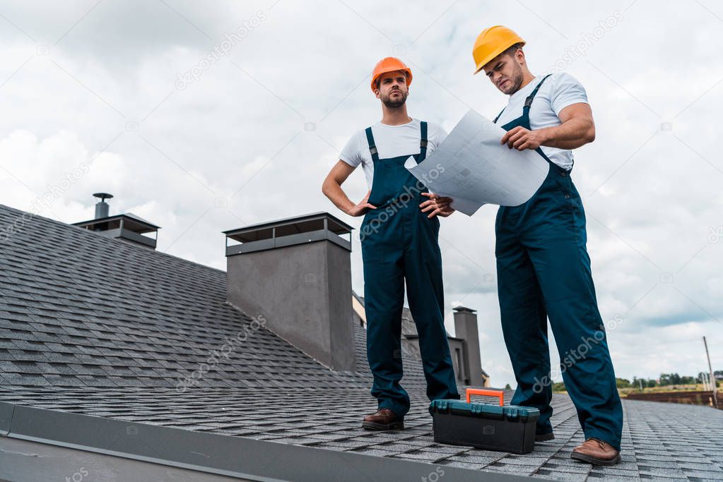 architect standing on roof with hands on hips near coworker with paper 