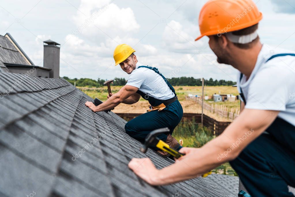 selective focus of happy repairman looking at coworker on roof 