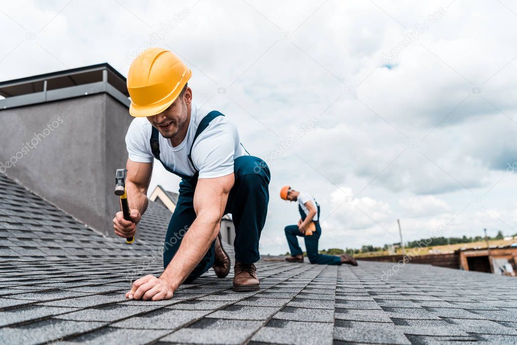 selective focus of handyman holding hammer while repairing roof near coworker 