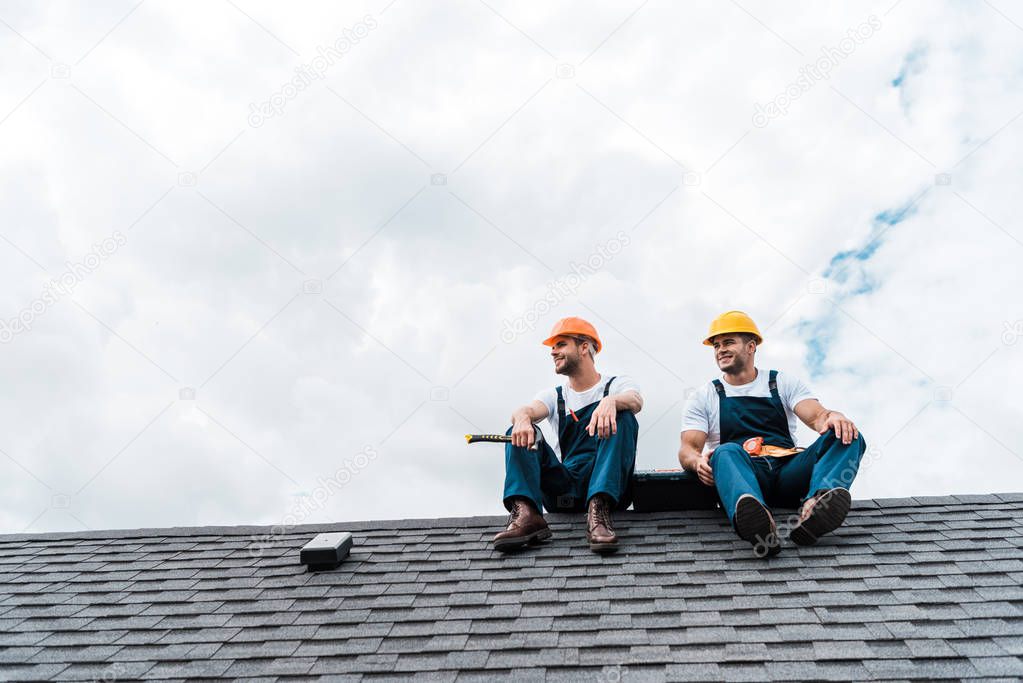 cheerful handymen in helmets sitting on rooftop 