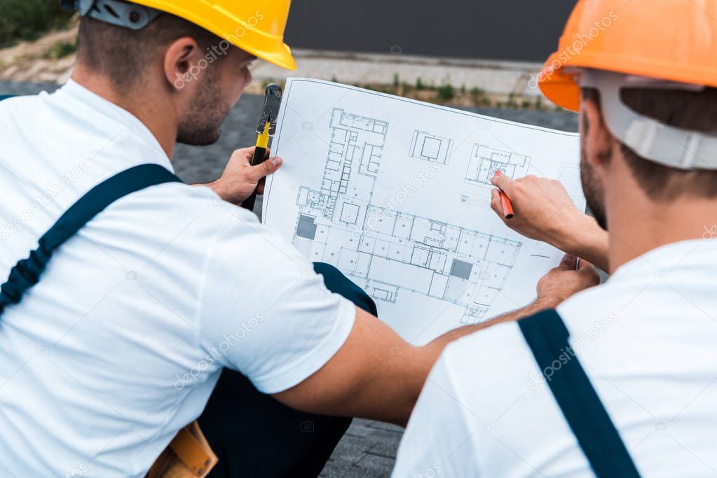 selective focus of builders in helmets looking at blueprint 