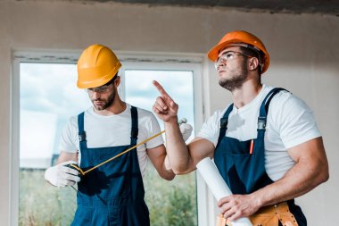 yakışıklı handyman parmak ile işaret iş arkadaşı yakınında ölçüm bandı bakıyor 