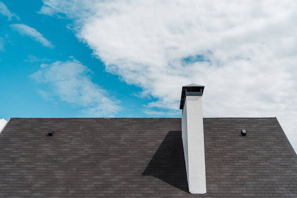 shingles on roof in new luxury house against blue sky with clouds 