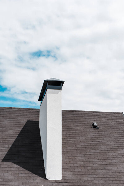 white chimney near shingles on roof in house against blue sky with clouds 