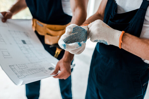 selective focus of man wearing gloves near coworker holding blueprint 