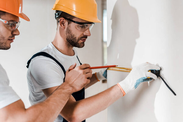 selective focus of handymen in goggles measuring wall with measuring tape 