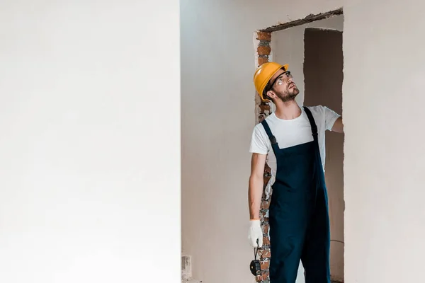 handsome repairman in gloves holding measuring tape and looking at wall