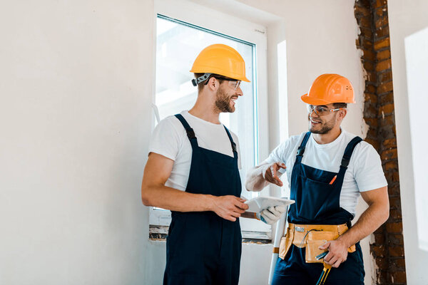 cheerful repairman in goggles looking at coworker while holding digital tablet  