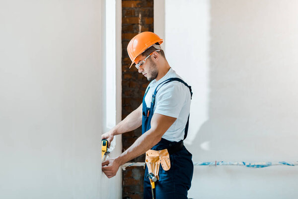 handsome repairman holding yellow measuring tape near wall  