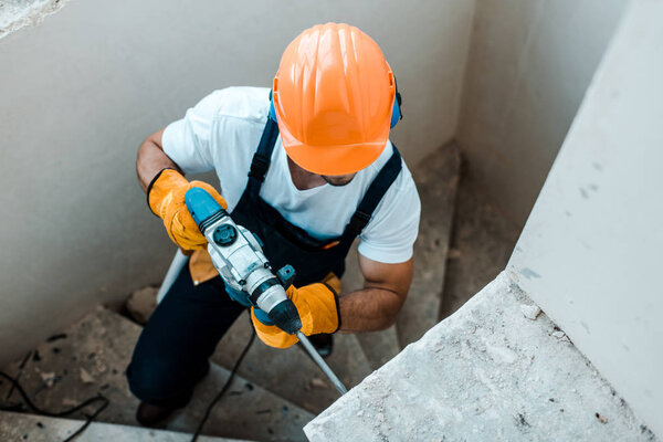 overhead view of workman in uniform and yellow gloves using hammer drill 