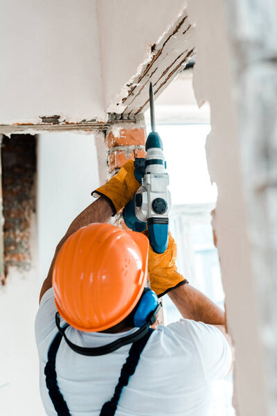 back view of handyman using hammer drill on wall 