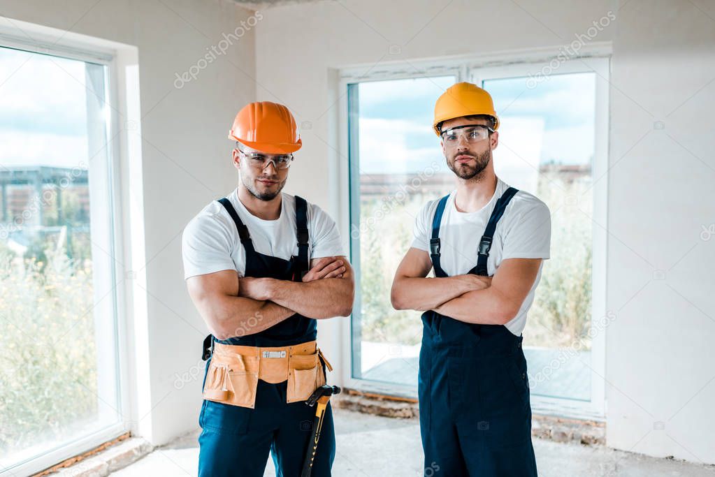 handsome handymen in helmets and goggles standing with crossed arms 