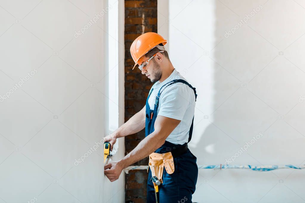 handsome repairman holding yellow measuring tape near wall  