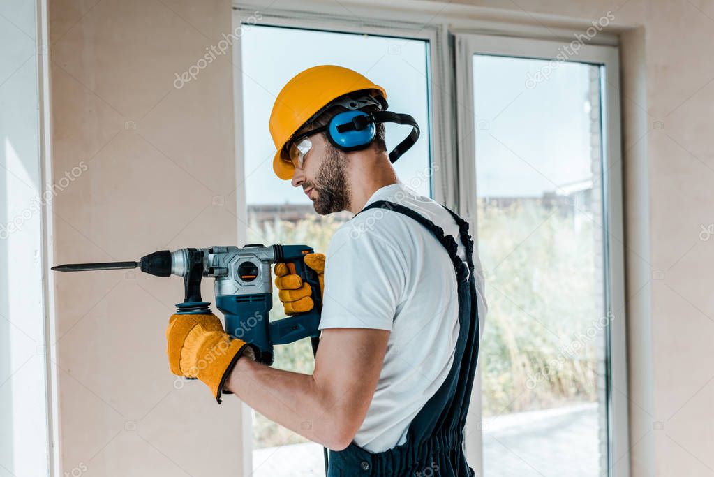 handyman in helmet and yellow gloves using hammer drill 