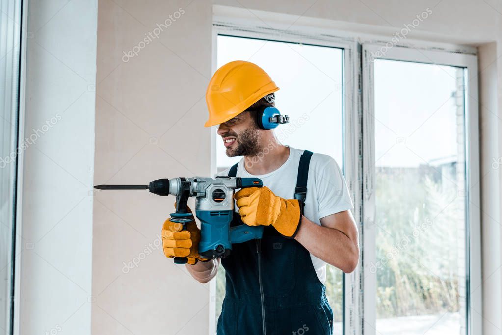 handyman in uniform and yellow gloves using hammer drill 
