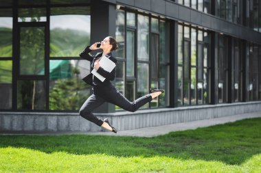 akıllı telefon konuşurken ve dizüstü bilgisayar tutarak güzel iş kadını levitating