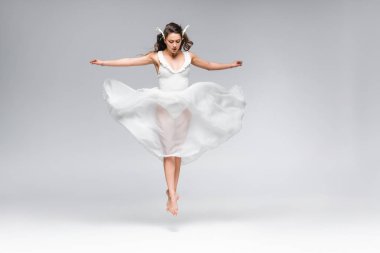 gri arka planda dans ederken beyaz elbiseli genç çekici balerin atlama