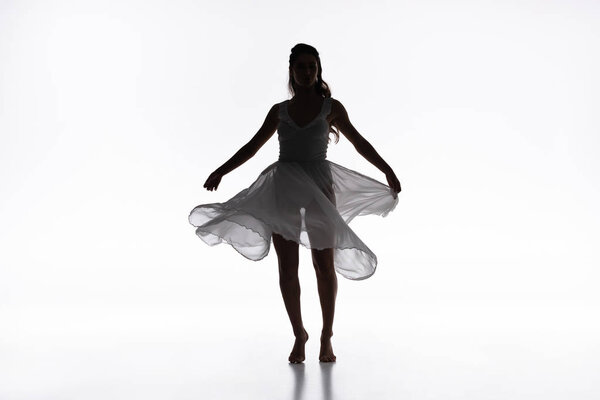 Young graceful ballerina in white dress dancing on grey background