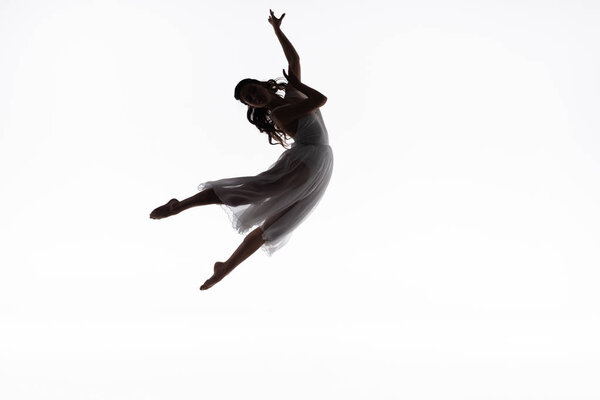 Молодая изящная балерина прыгает, танцуя изолированно на белом
