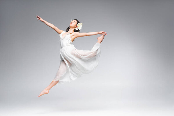 Beautiful young ballerina in white dress dancing on grey background