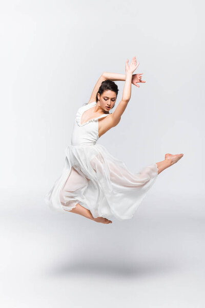 beautiful young ballerina dancing in white dress on grey background