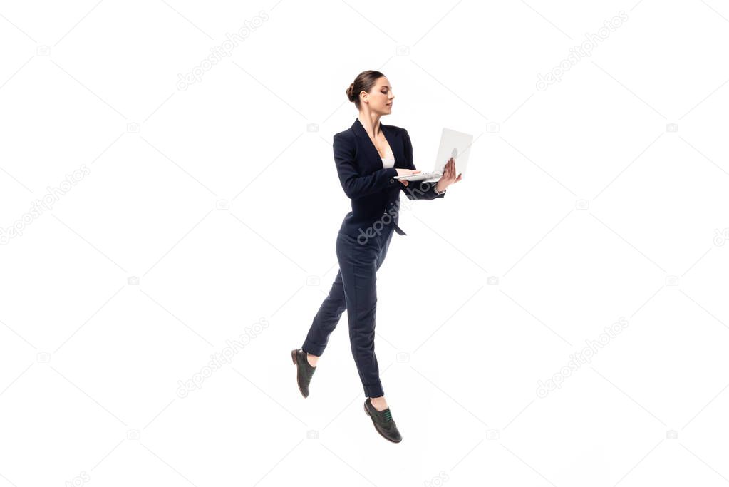 beautiful graceful businesswoman in black formal wear dancing while using laptop isolated on white