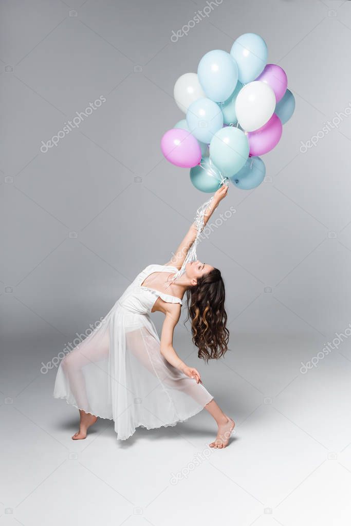 graceful ballerina in white dress dancing with festive balloons on grey background