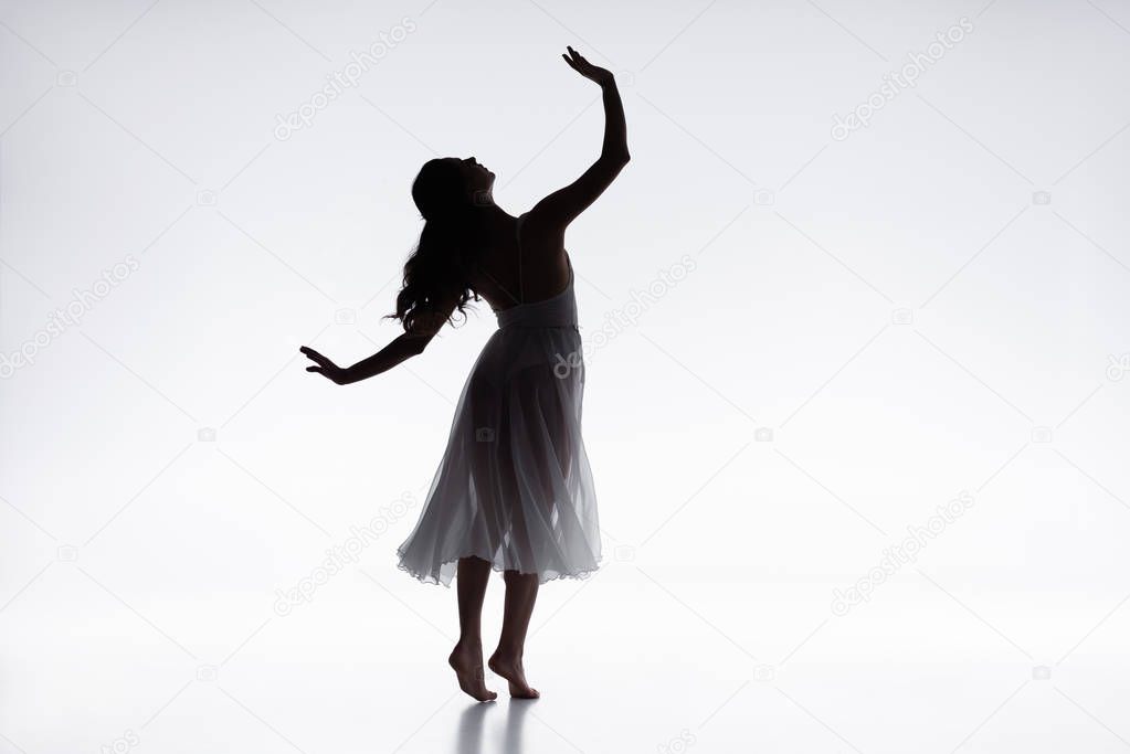 graceful, elegant ballerina in white dress dancing on grey background