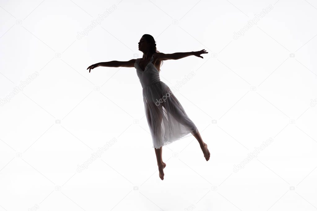 young, graceful ballerina jumping while dancing on white background