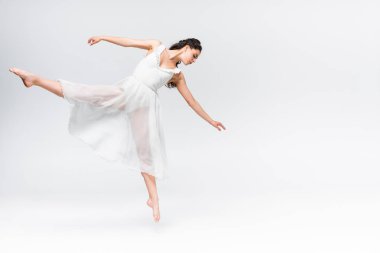 attractive young ballerina dancing in white dress on grey background clipart