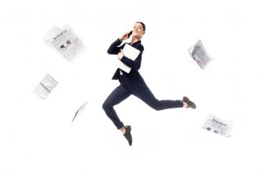 gülümseyen iş kadını akıllı telefon konuşuyor ve beyaz izole etrafında uçan gazeteler ile çevrili levitating sırasında dizüstü bilgisayar tutarak
