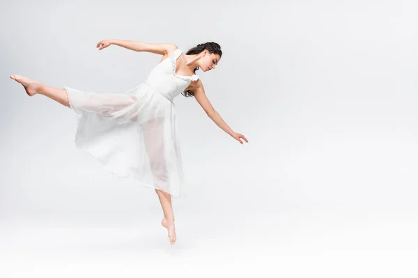 迷人的年轻芭蕾舞女郎在灰色背景上穿着白色连衣裙跳舞 — 图库照片
