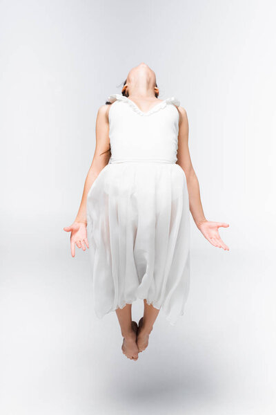 молодая, изящная балерина в белом платье танцует на сером фоне

