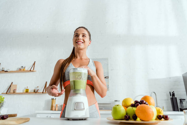 low angle view of cheerful woman near blender with smoothie 