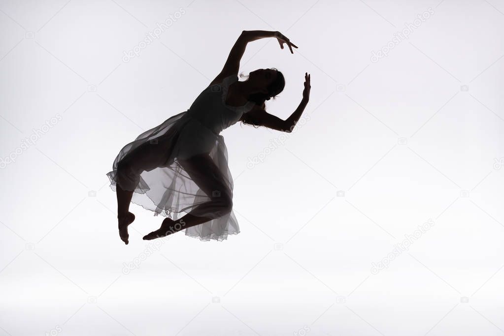 young graceful ballerina jumping in dance on grey background