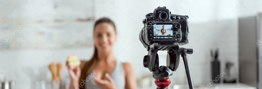 panoramic shot of digital camera with happy woman holding half of apple and gesturing on screen 
