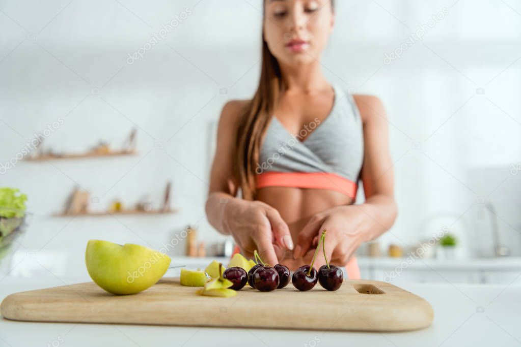 selective focus of woman standing near apples and sweet cherries on cutting board 