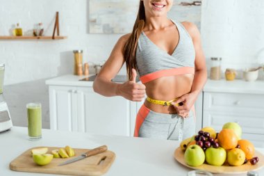 meyvelerin yanında bel ölçme ve başparmak gösteren genç kadının kırpılmış görünümü