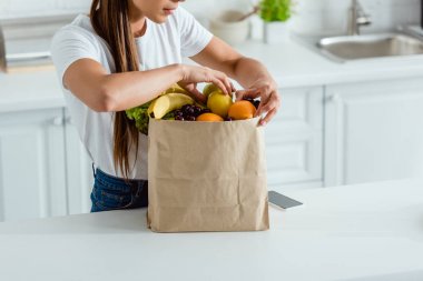 cropped view of woman touching organic fruits in  paper bag  clipart