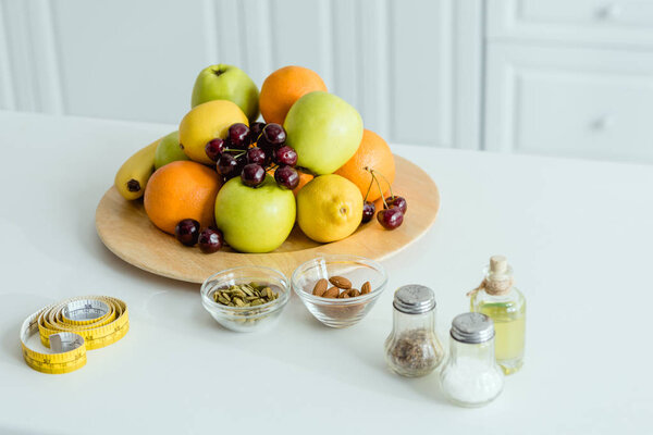 tasty and ripe fruits on plate near measuring tape on table 