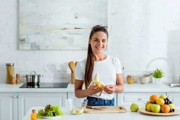 Felice Ragazza Taglio Banana Sul Bordo Peeling Vicino Frutti Gustosi — Foto Stock