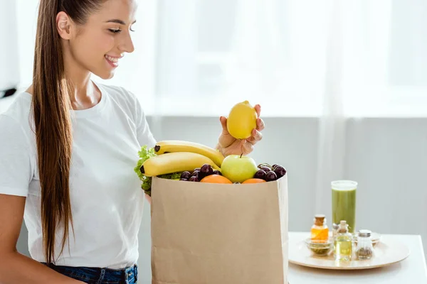选择性的焦点快乐的女人拿着柠檬附近的纸袋与水果 — 图库照片