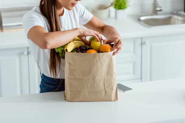 cropped view of woman touching organic fruits in  paper bag 