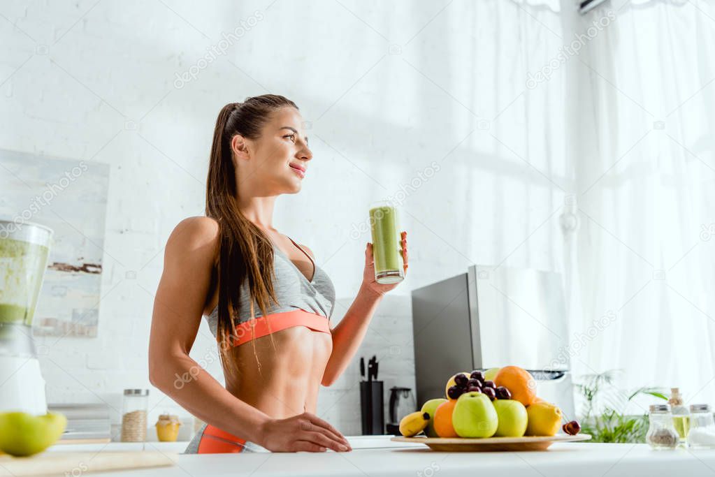 low angle view of attractive and happy woman holding glass with green smoothie 