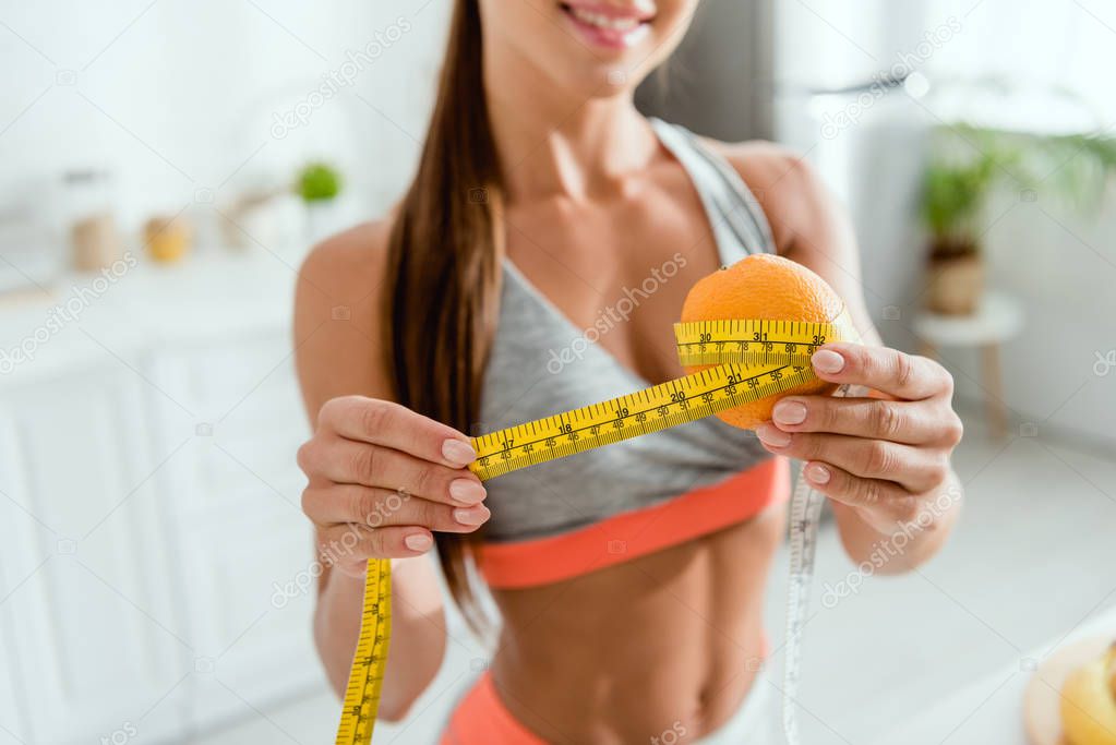 cropped view of cheerful young woman measuring orange 