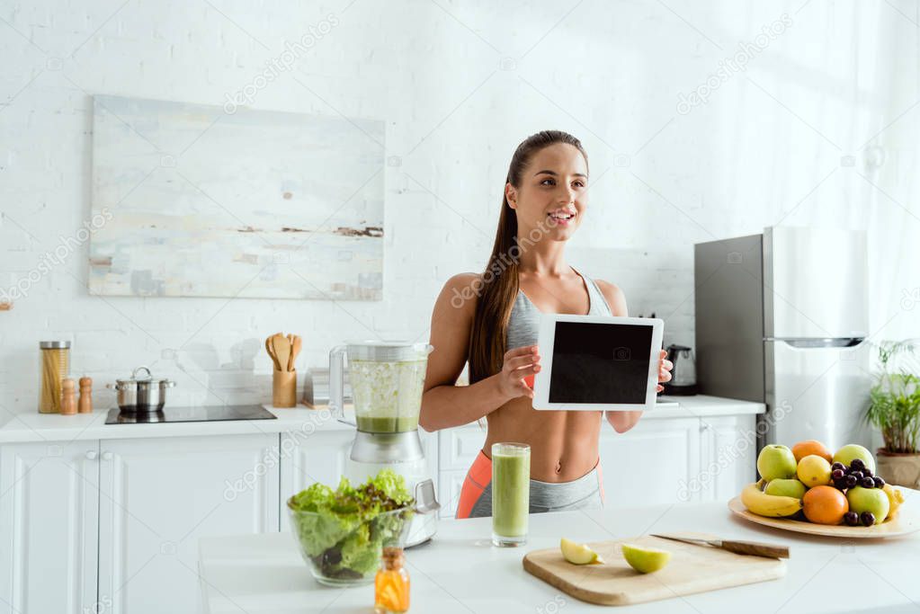 happy woman holding digital tablet with blank screen in kitchen 