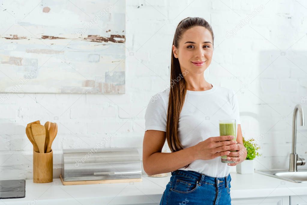 happy girl smiling while holding glass with green smoothie 