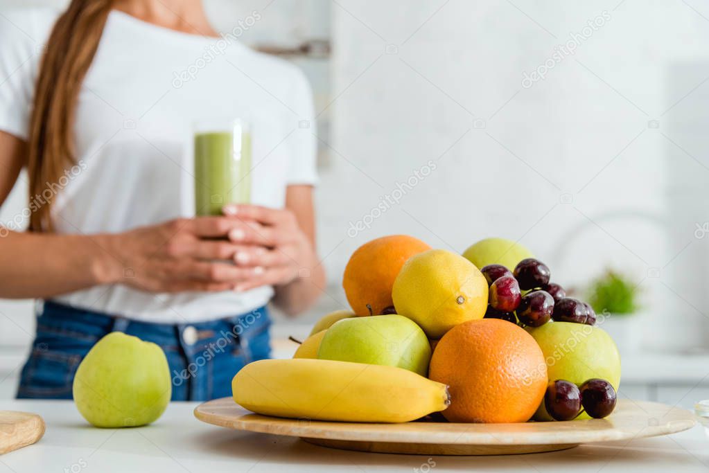 selective focus of ripe delicious fruits near girl holding glass with green smoothie 