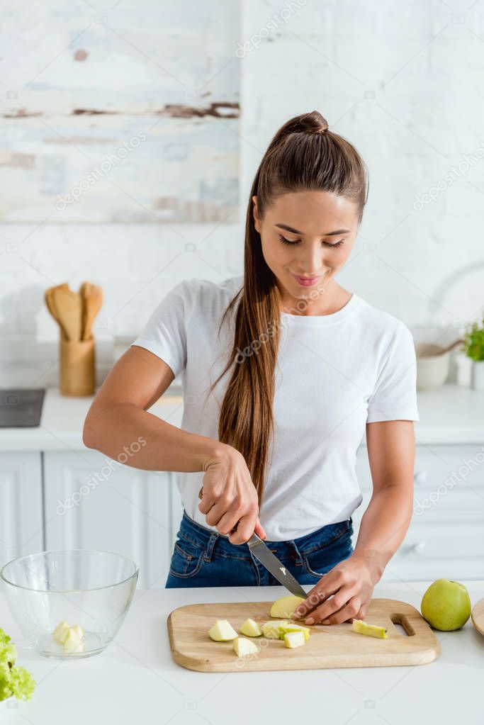 Cheerful young woman cutting green apple on chopping board