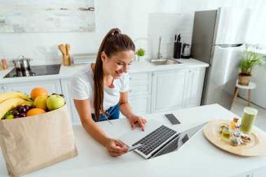 boş ekranile akıllı telefon yakınında dizüstü bilgisayar kullanarak neşeli kadın 